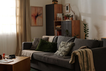 Stylish living room featuring green and gray furnishings with modern art on walls. Warm interior with natural light streaming, plants, and various decorative items enhancing the ambiance