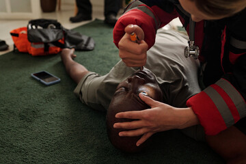 Emergency responder delivering critical first aid to unconscious individual lying on green carpet...