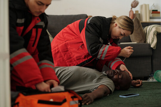 Emergency responders assisting unconscious African American male on living room floor. One responder checking pulse while another prepares medical equipment