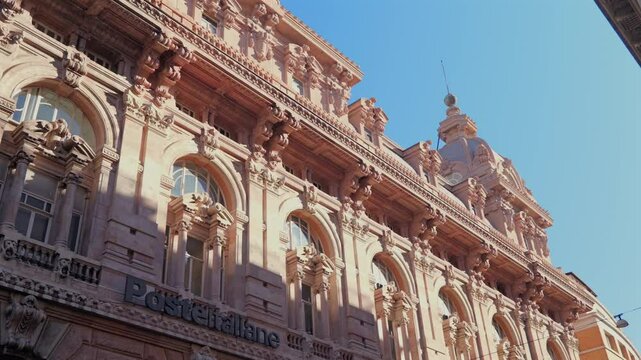 Low-angle view of the ornate Poste Italiane building in Genoa&rsquo;s Piazza De Ferrari, Italy, featuring sculpted arches, dome and classical facade in natural sunlight
