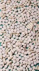 Many white pills and capsules filling the frame on a teal background