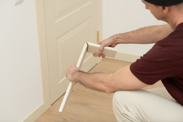 A craftsman is carefully measuring and cutting a wooden piece to create a custom door frame in a...