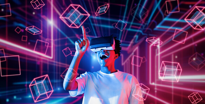 Smart teenager wearing VR glasses and excited about geometric shape. African gamer wearing casual cloth and surrounded with glowing light color while using augmented reality technology. Ingenuity.