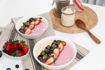 Presented by fruits putting yogurt toppings with strawberry, berry, oats, raisins and chia seed decorated by peppermint in white blow. Pink background. Set of healthy dairy product choice. Pecuniary.