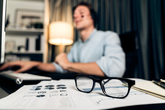 Call center consulting with customers on headphones on monitor in business paragraph with typing on pc with dynamic data marketing analysis planning at modern home office at night time. Pecuniary.