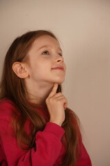 Fototapeta premium The girl thoughtfully touches her chin with her index finger, pondering her next move. The pose conveys a sense of deep reflection and curiosity. Her expression reveals a moment of contemplation.