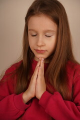 Naklejka premium A young girl with long red hair clasps her hands together as if in prayer. Her calm expression and flowing hair evoke innocence and peace. A tender and sincere moment is beautifully captured.
