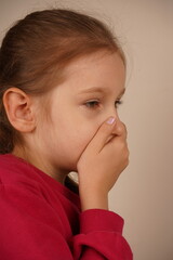 A frightened girl with a ponytail places her hand over her mouth, as if silencing herself from...