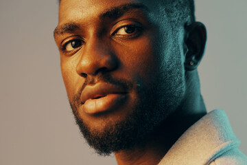 Obraz premium Portrait of a confident Black male model with a stylish haircut, showcasing warm skin tones and thoughtful expression, against a soft gradient backdrop