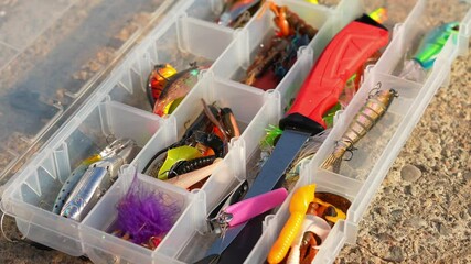 Angler tackle box with artificial fishing gear on the wooden rock surface. Accessories for fishing selective focus close up. Crankbaits treble lure or spoons, jigs spinners, soft plastics and swimbait