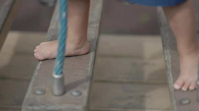 Happy little child barefoot stepping climbing rope bridge at playground step by step. Child steps climbs rope bridge adding excitement of playground adventures Child stepping rope bridge