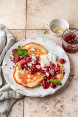 Homemade pancakes with yoghurt, berries and raspberry jam. Maslenitsa or Pancake day breakfast on beige tile background