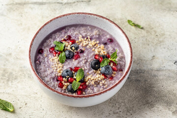 Wholegrain oatmeal porridge with blueberries, pomegranate seeds and nuts on textured background,...