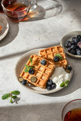 Waffles with fresh blueberries and cream in bright morning light. Healthy food, breakfast. Waffles with berries.