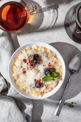 Rice porridge with blueberries, dried raspberries and caramel sauce on a table, hot and healthy breakfast with tea. Bright morning light