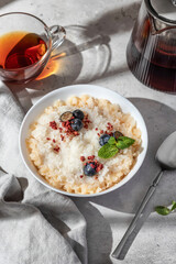 Rice porridge with blueberries, dried raspberries and caramel sauce on a table, hot and healthy breakfast with tea. Bright morning light