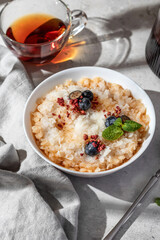 Rice porridge with blueberries, dried raspberries and caramel sauce on a table, hot and healthy breakfast. Bright morning light