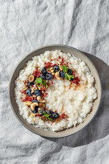 Rice porridge with blueberries, dried raspberries and nuts on a linen tablecloth, hot and healthy breakfast isolated. Bright morning light