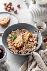 Wholegrain oatmeal porridge with caramelized pear, nuts and honey on white table, healthy food for breakfast