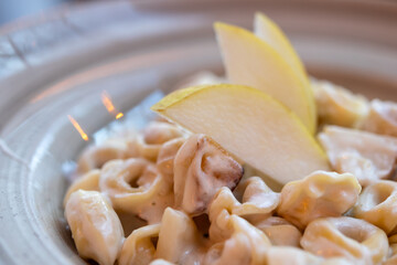 Cinque Terre Tortellini Delight. Close-up shot of creamy tortellini pasta with slices of pear, showcasing the texture and flavors of Italian cuisine.