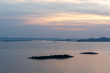 Obraz premium Peaceful coastal panorama with small islands and calm sea at dusk, highlighted by colorful sunset. Concept of natural beauty, serenity, and remote getaway destinations.
