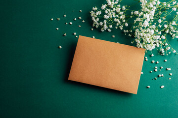 Brown envelope on a green background with white gypsophila flowers. Top view, flat lay, mockup
