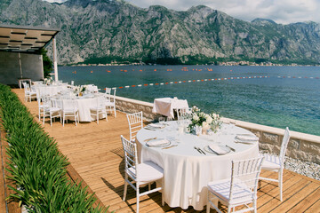 Round tables set on a wooden deck in a garden overlooking the sea