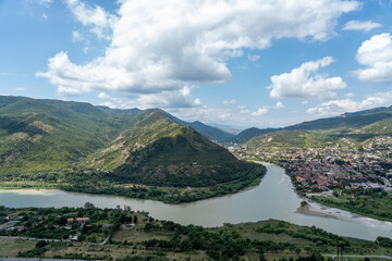 Charming Riverside Town Nestled Between Green Hills
A picturesque view of a peaceful riverside town with red-roofed buildings. The river branches into two, surrounded by lush green hills and majestic 