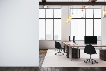 Modern office workspace with wooden desks, black chairs, and computers, featuring large windows and hanging lights. Blank white wall for mockup. 3D Rendering