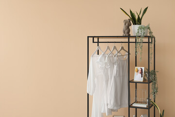 Shelving unit with clothes, accessories and houseplants near beige wall