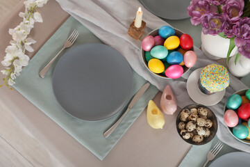 Festive table serving with painted eggs, flowers and burning candle for Easter celebration, top view