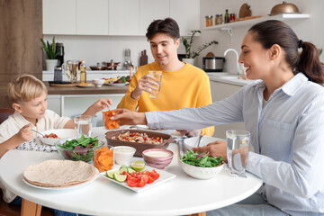 Cute little boy and his parents eating Fajita with nachos at table in kitchen