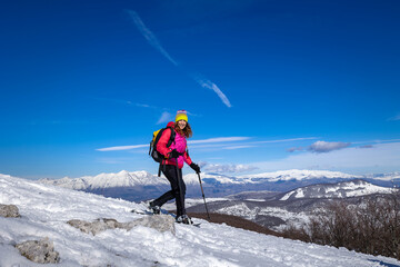 Active sporty woman walking on the snow wearing snowshoes, in the background the snowy mountains of a winter mountain landscape.