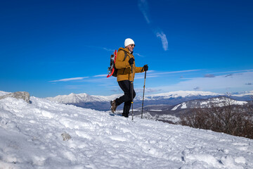 Active sporty man walking on snow wearing snowshoes, in the background snowy mountains of a winter mountain landscape.