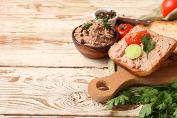 Bowl of tasty pate with toasts, parsley, tomato and onion rings on light wooden background
