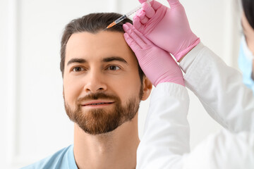 Young man receiving injection for hair growth at trichologist's office, closeup