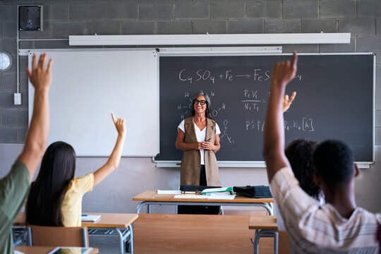 Rear view of a student in the classroom raising her hand to ask a question during class. A female high school student asks the teacher a question. Selective focus. High quality photo