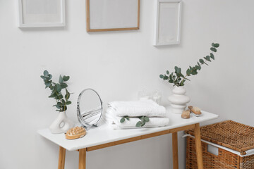Vases with eucalyptus branches, mirror and towels on table in bathroom