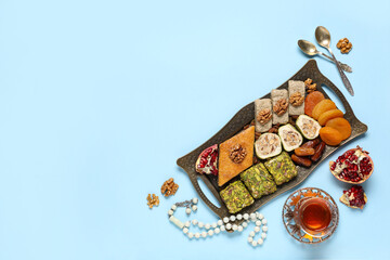Composition with delicious Eastern sweets, cup of tea and tasbih on color background. Ramadan...