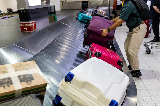 Traveler collecting own luggage from the airport terminal carousel conveyer belt in arrival area