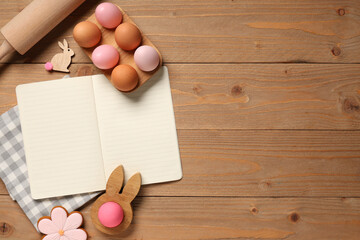 Composition with blank recipe book, beautiful Easter eggs and rolling pin on wooden background
