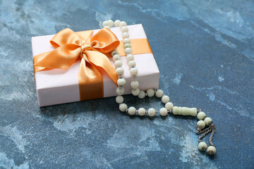 Tasbih and gift box on blue grunge background. Ramadan celebration