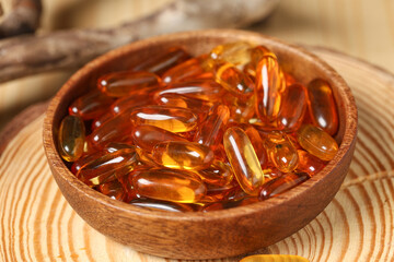 Wooden board with bowl of fish oil capsules, closeup