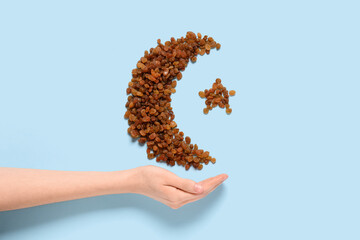 Female hand with crescent and star made of tasty raisins on color background. Ramadan celebration