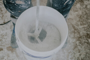 A young man mixes putty with a construction mixer in a bucket.