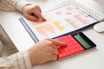 Female accountant with calculator, keyboard and financial graphics at table in office