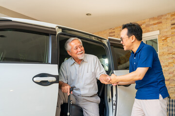 Asian man caregiver or taxi driver helping senior man patient get in the car to get to medical...