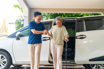 Asian man caregiver or taxi driver helping senior woman patient get in car to get to medical...