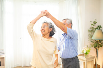 Obraz premium Happy Asian family senior couple enjoy and fun leisure activity lifestyle dancing together in living room. Healthy elderly husband and wife relaxing at home. Aged people mental healthcare concept.