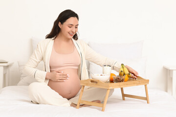 Young pregnant woman with tasty breakfast in bedroom